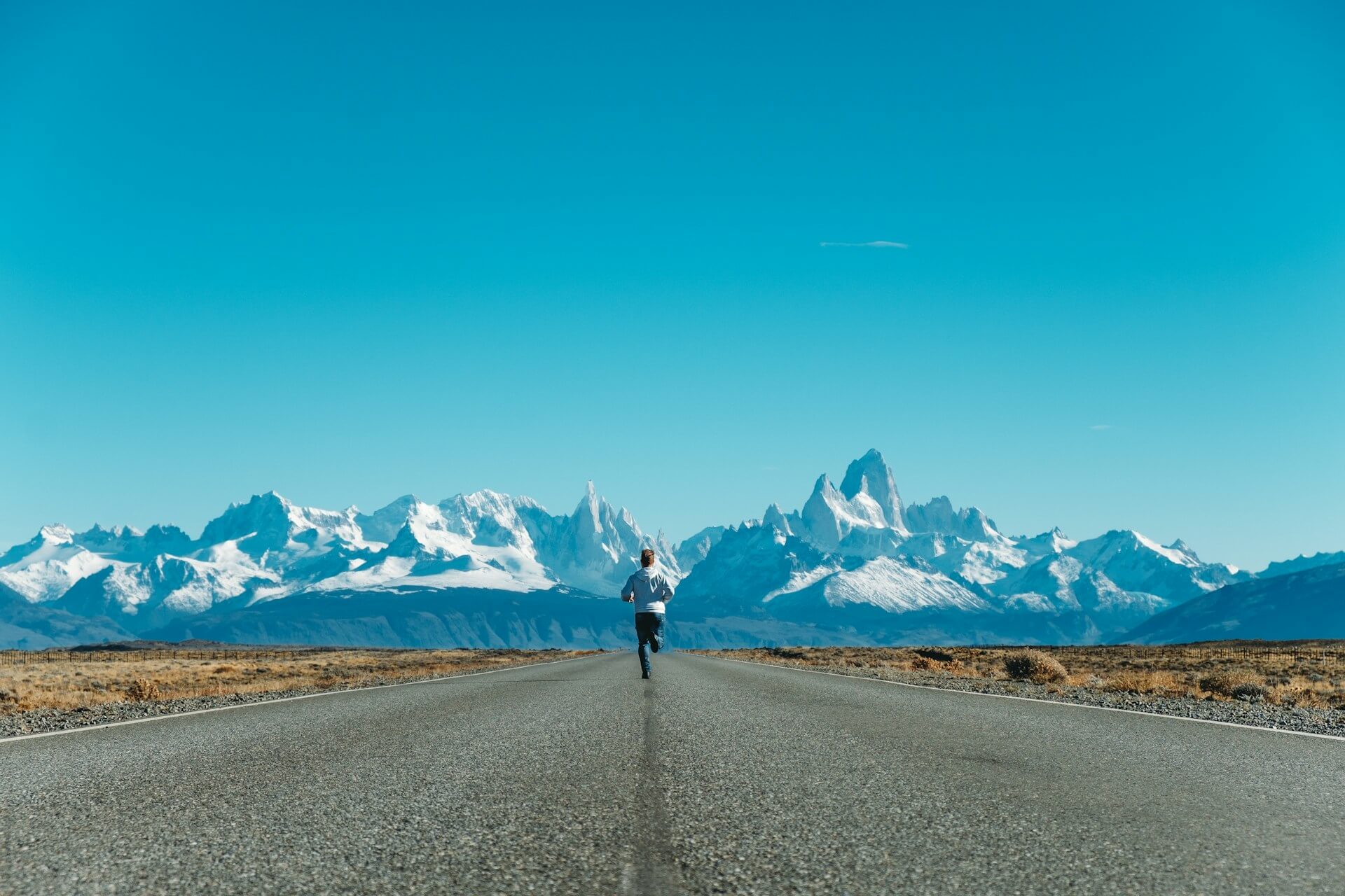 Runner in stunning landscape of snowy mountains and clear blue sky