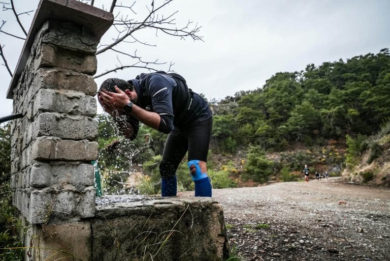 Trail runners in a trail running race, one soaking head under a tap