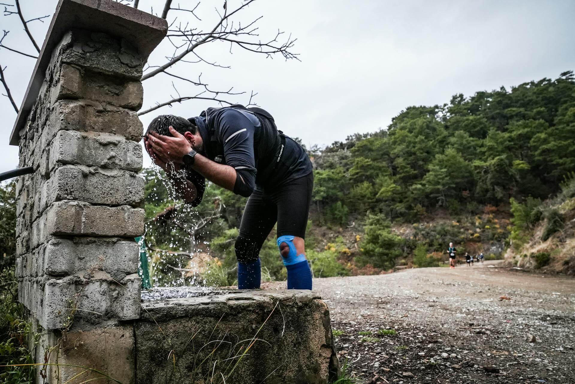 Trail runners in a trail running race, one soaking head under a tap